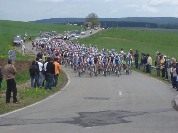 Een groot peloton wielrenners op de weg langs het huis.