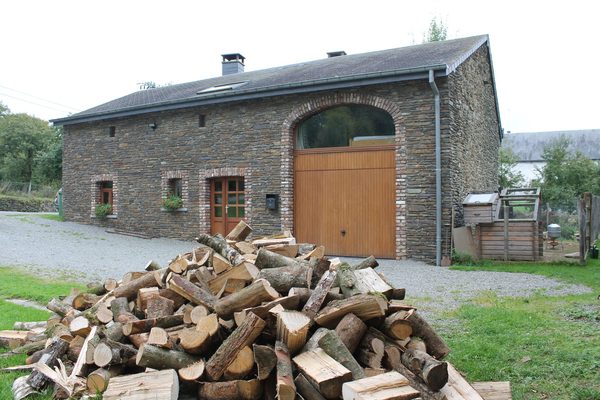 De natuurstenen hoeve met de grote groene poort, met een stapel openhaardhout ervoor.