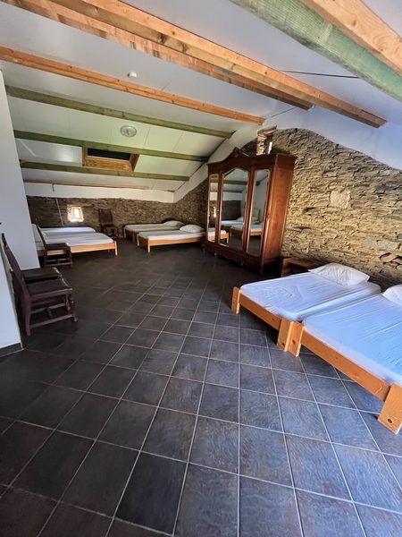 Een slaapzaal met bedden onder het balkenplafond, tegen de natuurstenen muur.